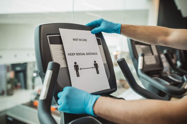 Affixing social distance sign to treadmill with gloves