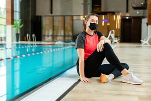 Girl in workout clothes and mask sitting by the pool